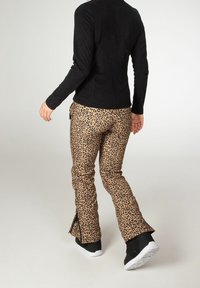Pantalones de leopardo en una paleta de colores beige y negro, con un corte ajustado y detalles de cremallera en los tobillos, combinados con una blusa de manga larga negra.