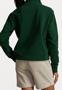 Felpa verde scuro con collo alto, maniche lunghe e vestibilità comoda, abbinata a pantaloni corti in corduroy beige con una trama a costine.