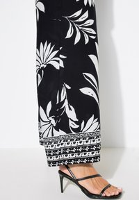 Černobílé květinové maxi šaty s listovým vzorem, se spodním lemem s komplikovanými detaily, nošeny s černými sandály na vysokém podpatku se šněrováním.