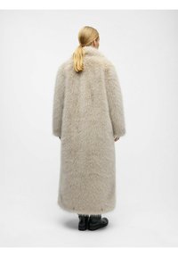 Lang beige faux fur frakke med højt krave, brede ærmer og fuldlængde design. Glat indre foring og støvler bæres nedenunder.