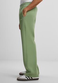 Groene, katoenen sweatpants met een trekkoord in de taille, zijzakken en een ontspannen pasvorm. Heeft subtiele branding bij de taille.