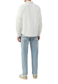 Chemise blanche à manches longues avec un col, associée à un jean en denim bleu clair. Le jean présente des poches arrière et une coupe droite, accompagné de baskets.