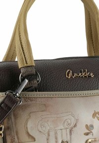 Braune und beige Handtasche aus strukturiertem Leder mit geprägten Details, Schulterriemen und goldfarbenen Beschlägen. Markenname vorne eingraviert.