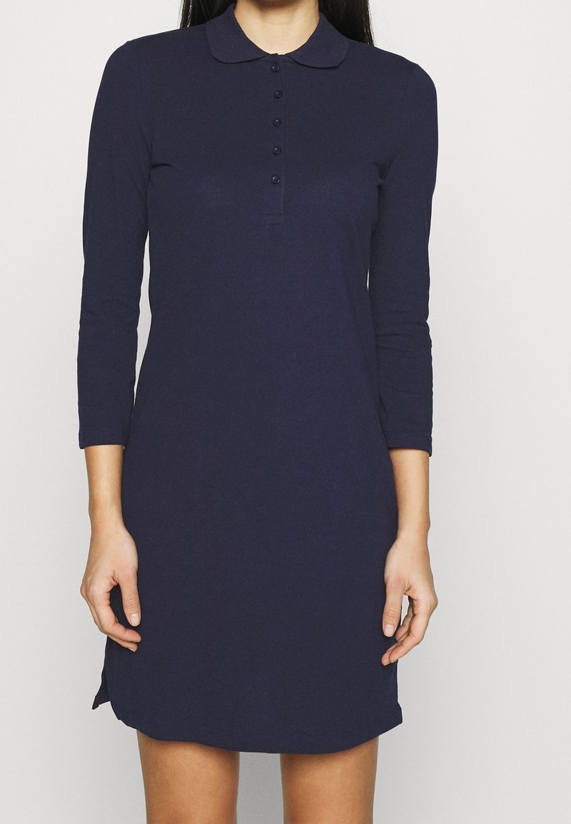 Mörkblå långärmad poloklänning med krage, som har en knappslå och sidokilar längst ner. Slätt, stretchigt tyg.