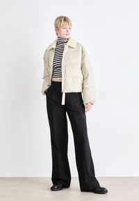 Doudoune beige pâle avec un col en fausse fourrure douce et de couleur claire. Associée à un pantalon large noir et un haut court à rayures.