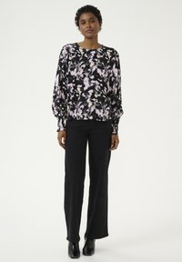 Top floreale in nero, rosa e crema, con maniche lunghe e vestibilità rilassata; abbinato a pantaloni neri a vita alta e stivali alla caviglia.