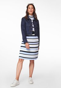 Denim-Cropped-Jacke über einem figurschmeichelnden, plissierten Kleid mit blauen, weißen und schwarzen Streifen; kombiniert mit weißen Sneakern und leichten Accessoires.