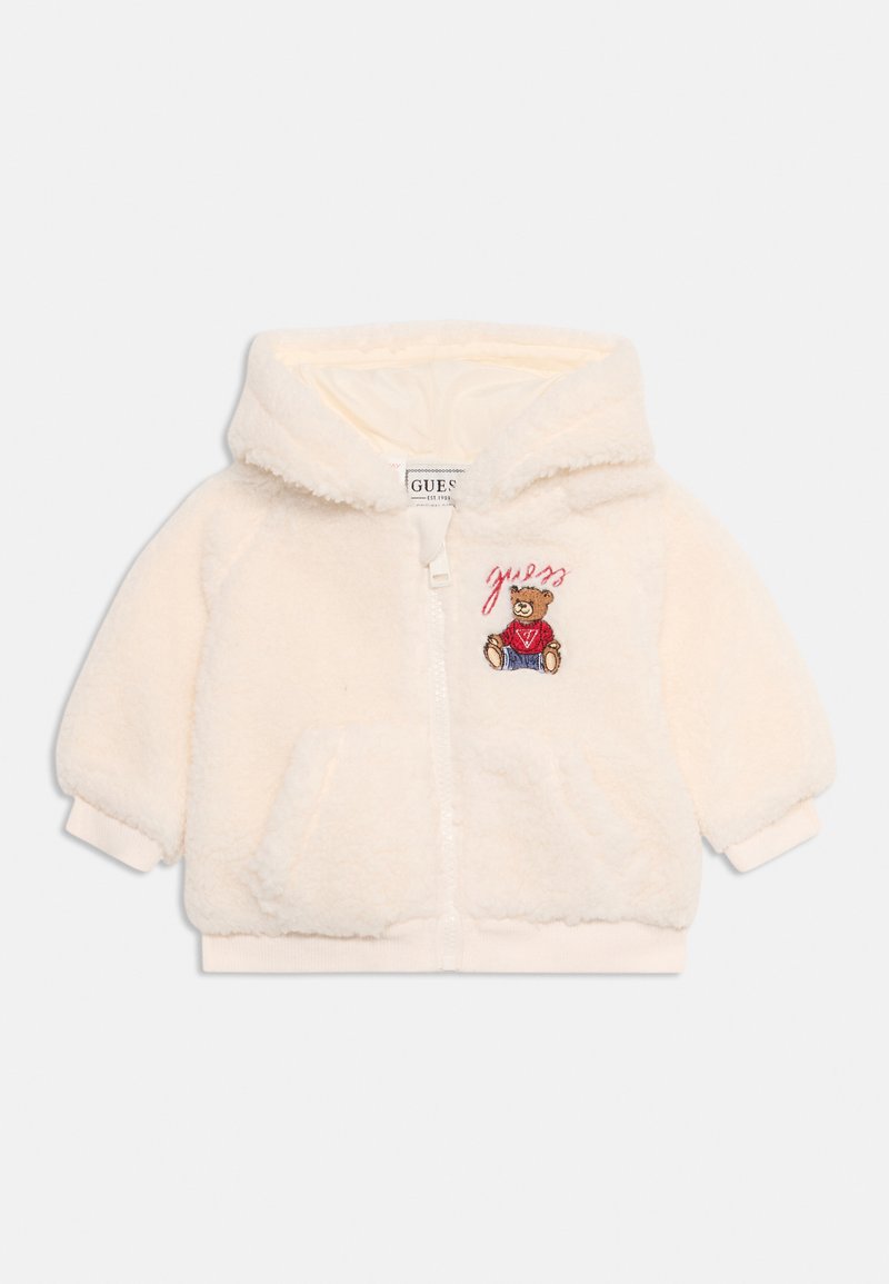 Felpa per bambino di colore crema, morbida e con zip frontale, tasche a marsupio e un ricamo di un orsetto che indossa un maglione rosso con il testo "guess" sopra.
