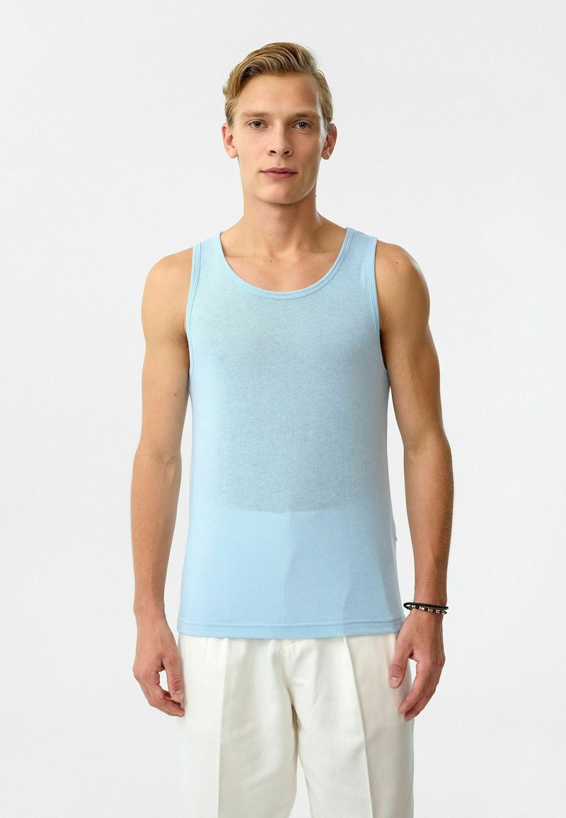 Lichtblauw katoenen tanktop met ronde halslijn en slim fit, gecombineerd met witte losse broek, gedragen door een model.