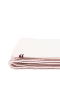 Couverture pliée en tissu rose clair, texture douce, forme rectangulaire, avec une petite étiquette logo comportant des accents rouge, blanc et bleu.