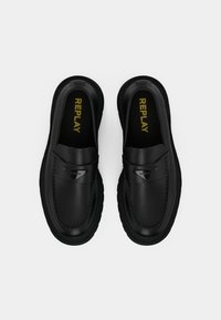 Sorte slip-on sko med en glat læderoverdel, tekstureret sål og et sølvfarvet dekorativt accent. Indvendig branding i gul.