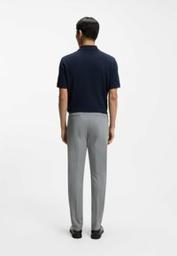 Granatowa koszulka polo z klasycznym kołnierzykiem, zestawiona z jasnoszarymi spodniami. Dopasowany krój z delikatnym połyskiem, a dopełnieniem stroju są czarne buty.