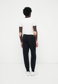 Zwarte sweatpants met elastische boorden en tailleband, gecombineerd met een eenvoudig wit t-shirt. Het model draagt witte sneakers.
