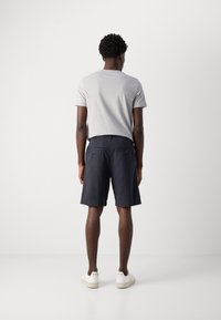 Tricou gri cu mânecă scurtă, pantaloni scurți bleumarin cu buzunare la spate și adidași albi. Design minimalist și croială lejeră.