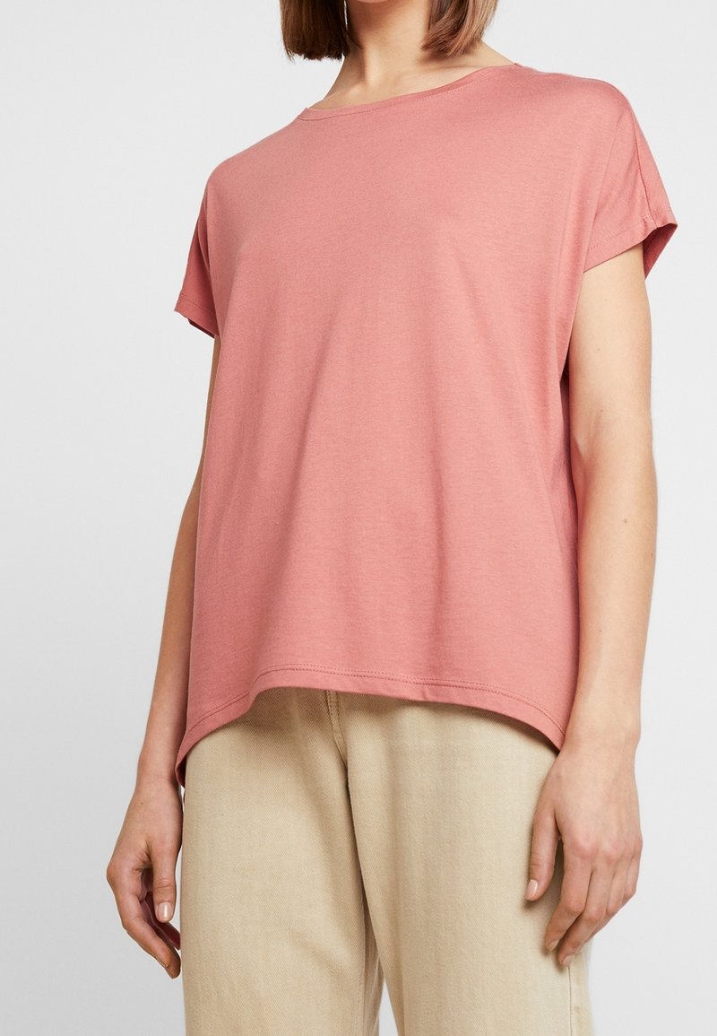 Camiseta de manga corta rosa claro con un ajuste holgado, escote redondo y tejido de algodón suave. Presenta un dobladillo recto y costuras mínimas.
