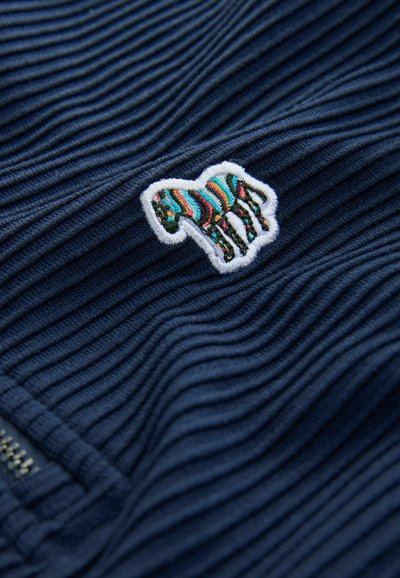 Il tessuto a trama navy presenta una toppa di zebra ricamata multicolore con un bordo bianco, posizionata su una superficie rigata.