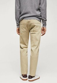 Pantalones de algodón beige con corte recto, que cuentan con dos bolsillos traseros, detalles cosidos, y se combinan con zapatillas blancas y marrones.
