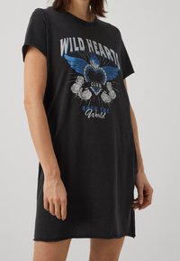 Robe t-shirt en coton noir à manches courtes, ornée d'un imprimé graphique avec des ailes, un cœur et des roses en bleu et blanc. Fentes latérales à l'ourlet.