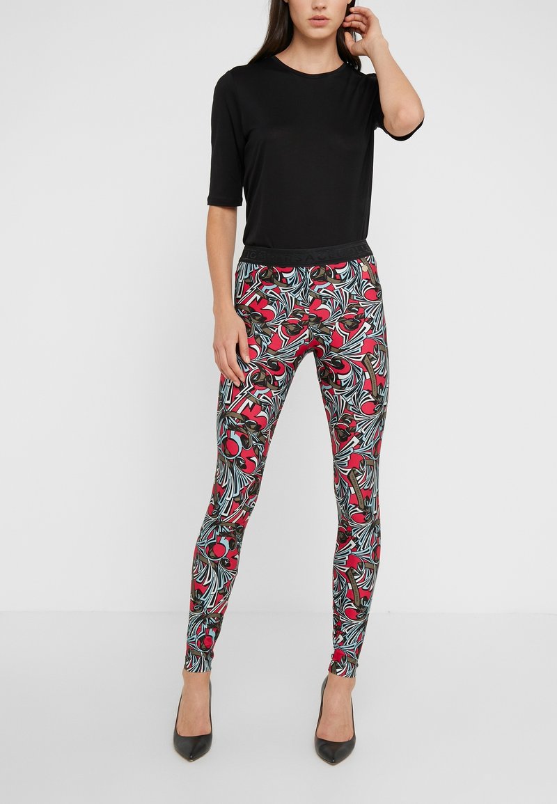 Svart kortärmad topp kombinerad med åtsittande leggings med ett livfullt mönster av blommor och löv i röda, gröna och blå nyanser. Svarta klackar.