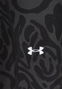 Primo piano di un tessuto mimetico nero e grigio scuro con il logo bianco di Under Armour e cuciture verticali visibili.
