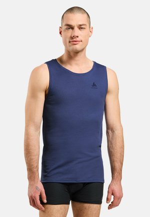 Man wearing a navy blue sleeveless athletic shirt and black shorts standing against a plain light background.