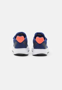 Zapatilla azul con parte superior de malla, entresuela blanca y suela negra. Presenta un acento naranja brillante en el talón y paneles laterales grises.