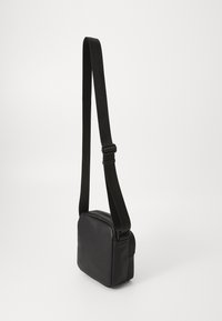 Black crossbody bag with a rectangular shape. Made of smooth material, features an adjustable strap and a zip closure. Minimalist design.