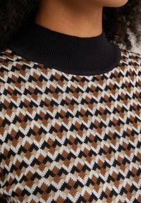 Stickad tröja med en svart ribbad krage, med ett geometriskt mönster i brunt, kräm och svart. Texturerad tyg med en lagerdesign.