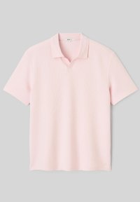 Polo rose clair à manches courtes avec col doux et petite encoche en V à l'encolure sur fond gris.