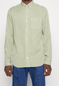 Camicia a maniche lunghe verde chiaro con colletto botton-down, taschino sul petto singolo e bottoni bianchi. Tessuto morbido e strutturato.