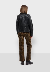 Černá kožená bunda s hladkou texturou, spojená s kalhotami s leopardím vzorem v odstínech hnědé a černé. Masivní černé boty na podpatku.