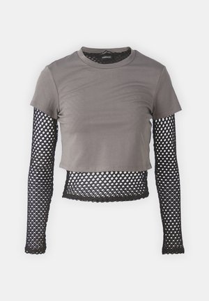 T-shirt grise court à manches courtes avec manches longues en maille noire, arborant un motif en diamant et un ourlet ondulé.