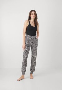 Juoda tanki palaidinė derinama su laisvomis baltomis kelnėmis, puoštomis juodu abstrakčiu raštu. Kelnėse yra elastinga liemens juosta ir rankogaliai.