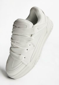 White sneaker featuring a chunky design, smooth leather upper, textured tongue, thick laces, and a rubber sole with ridges for grip.