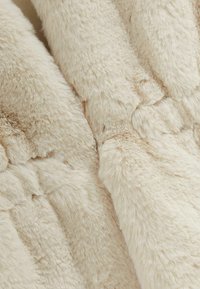 Tessuto in pelliccia artificiale color crema con una texture morbida e plussata. Presenta lunghezze variabili delle fibre di pelliccia che creano un aspetto caldo e accogliente.