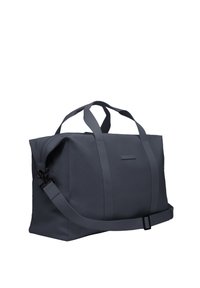 Sac fourre-tout en tissu gris avec doubles poignées et bandoulière réglable ; présente une texture lisse et une fermeture éclair, avec des détails minimalistes.