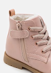 Růžová kotníková bota z umělé kůže s měkkou podšívkou, dekorativními zipy, copánkovými tkaničkami a růžově zlatými ozdobami. Gumená podrážka s dezénem.