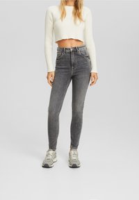 Vaqueros gris de tiro alto con corte ajustado, combinados con un suéter corto de canalé blanco y zapatillas grises con cordones blancos. Textura de tela suave.