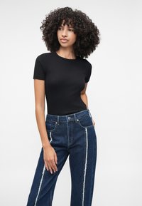 Top preto de mangas curtas caneladas, combinado com jeans azul de perna larga com riscas brancas verticais desgastadas e bolsos clássicos de denim.