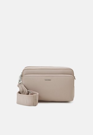 Nude crossbody taška vyrobená z hladkého materiálu, s dvěma zipovými přihrádkami, nastavitelným popruhem a diskrétním logem.