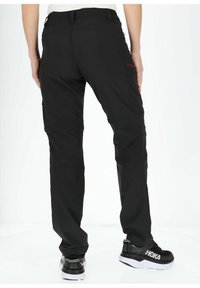 Black outdoor pants with a tapered design, featuring multiple pockets, subtle texture, and a zippered accent on the side. Black shoes with white sole.