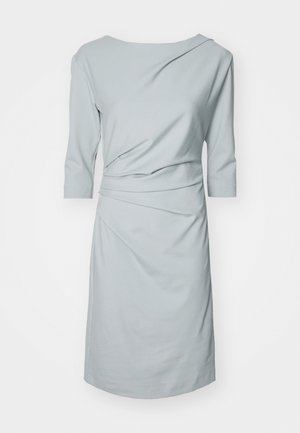 Lyseblå kjole laget av mykt stoff, med båthals, trekvartlange ermer og rynkede detaljer for en drapert effekt.