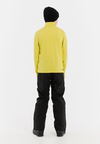 Geel langemouwen shirt met hoge kraag, gecombineerd met zwarte broek. Draag het met een zwarte gebreide beanie en stevige zwarte schoenen.