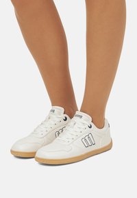 Sneakers bianchi in pelle con accenti blu navy, punta rotonda, suola in gomma e logo distintivo sui lati. Chiusura con lacci e collo imbottito.