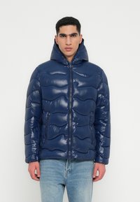 Jachetă puffer bleumarin cu un finisaj lucios, având un model ondulat capitonat, închidere cu fermoar și guler înalt cu glugă.
