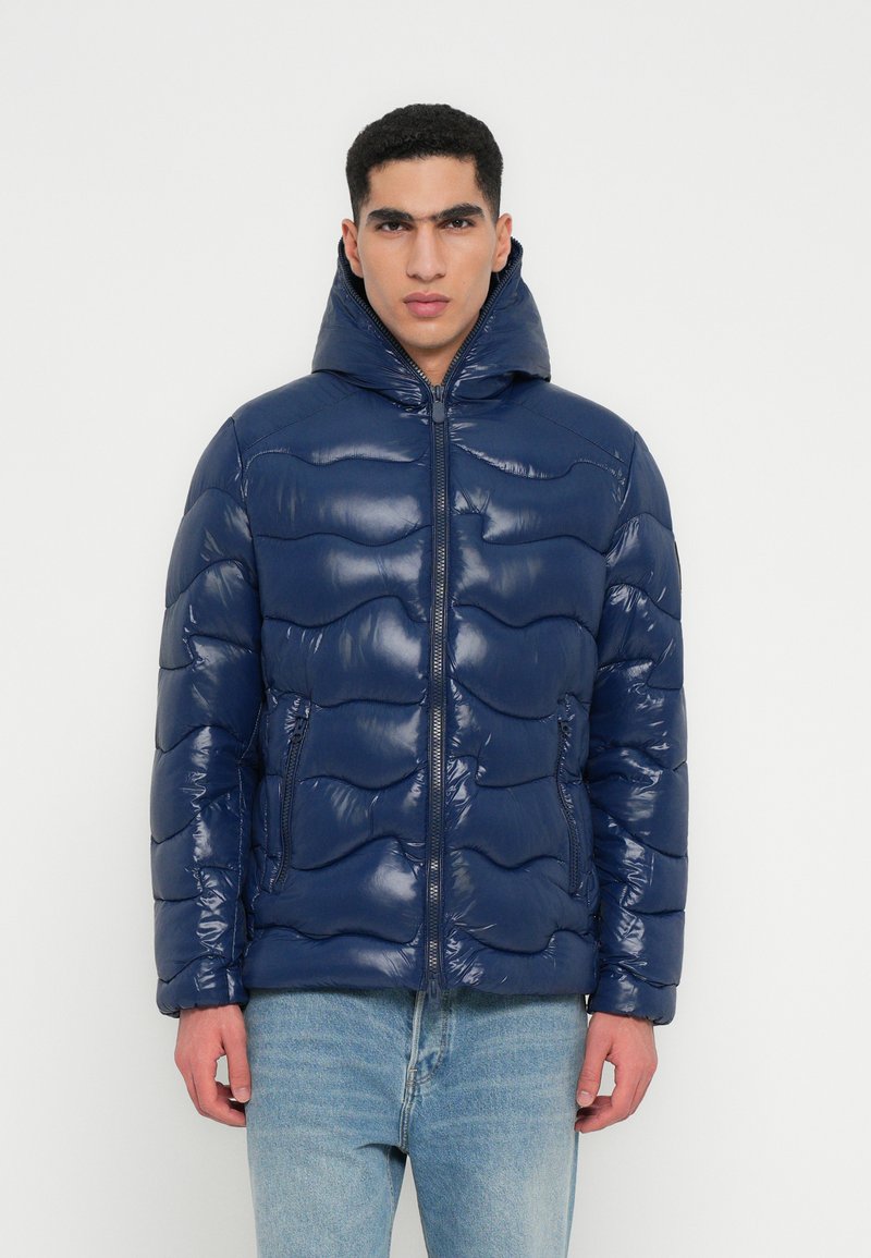 Jachetă puffer bleumarin cu un finisaj lucios, având un model ondulat capitonat, închidere cu fermoar și guler înalt cu glugă.