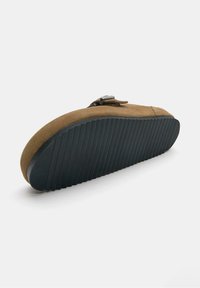 Brune ruskind slip-on sko med en tekstureret gummisål. Har en flad, rund tå og en rem med en spænde detalje over støvlen.