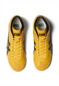 Žluté tenisky s černými a šedými akcenty, vybavené texturovanou semišovou špičkou a lehkým designem. Šněrování je žluté, součástí je také značený jazyk.