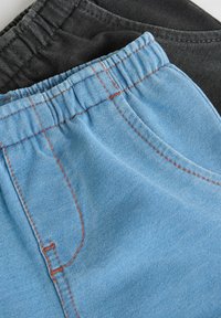 Två par byxor med elastisk midja: ett par ljusblå jeans med orange sömmar och ett par svarta i tyg. Båda har fickor och mjuka texturer.
