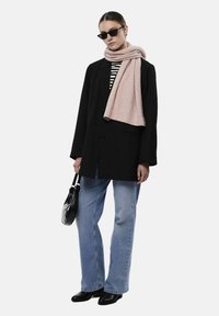 Blazer noir oversized, chemise rayée, jeans bleu clair, écharpe rose pâle, lunettes de soleil noires et petit sac à main noir ; look élégant et moderne.